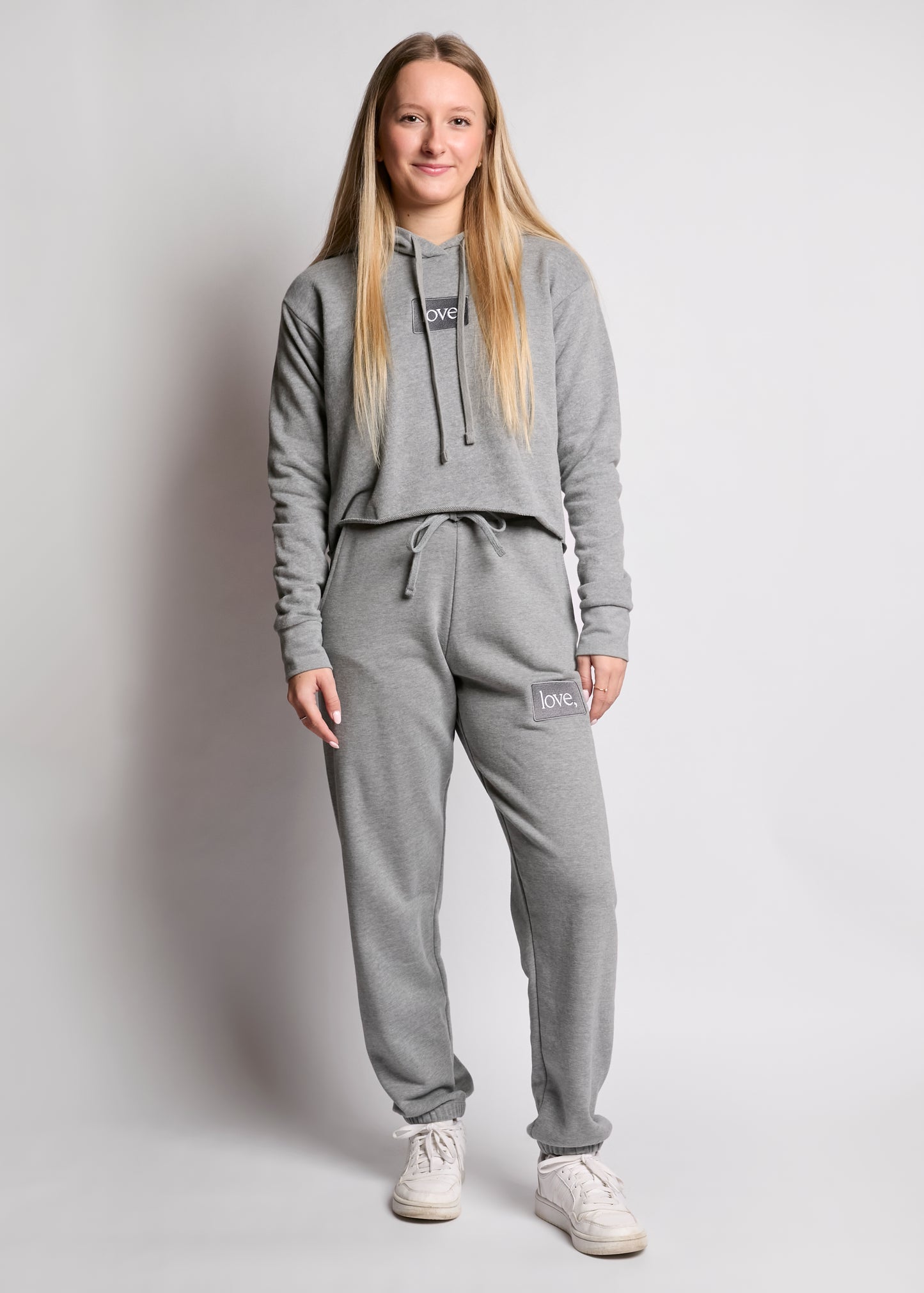 Person wearing a gray tracksuit with a brand logo on a plain background
