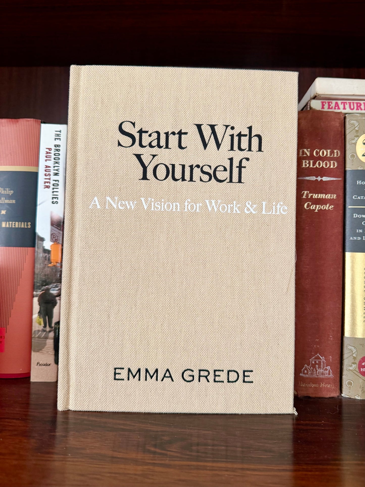 Book titled 'Start With Yourself' by Emma Grede on a wooden surface with other books in the background.