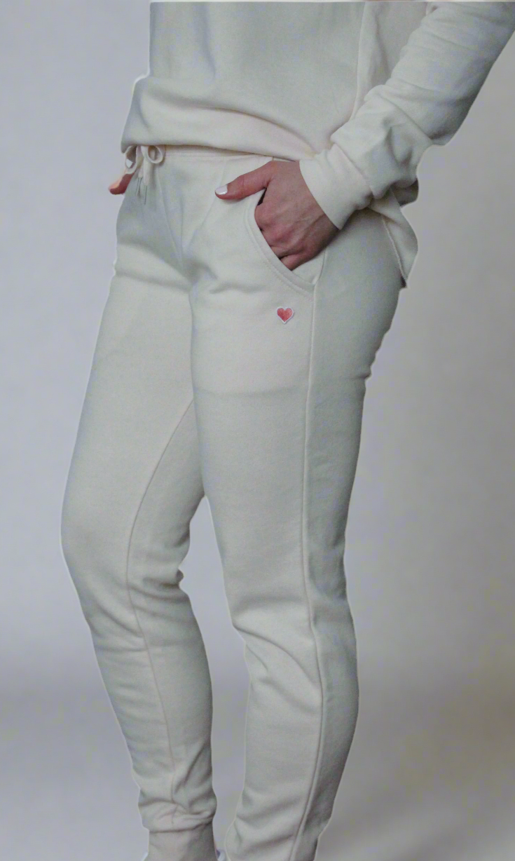 A person wearing a beige sweatshirt and sweatpants with a pink heart patch on the left hip. The clothing is made of fleece fabric.