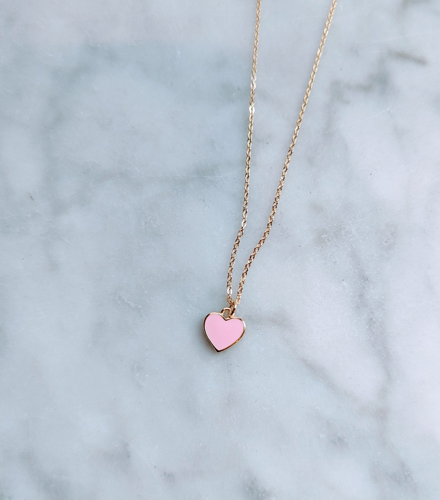 A gold-plated sterling silver necklace with a pink enamel heart pendant on a marble surface.