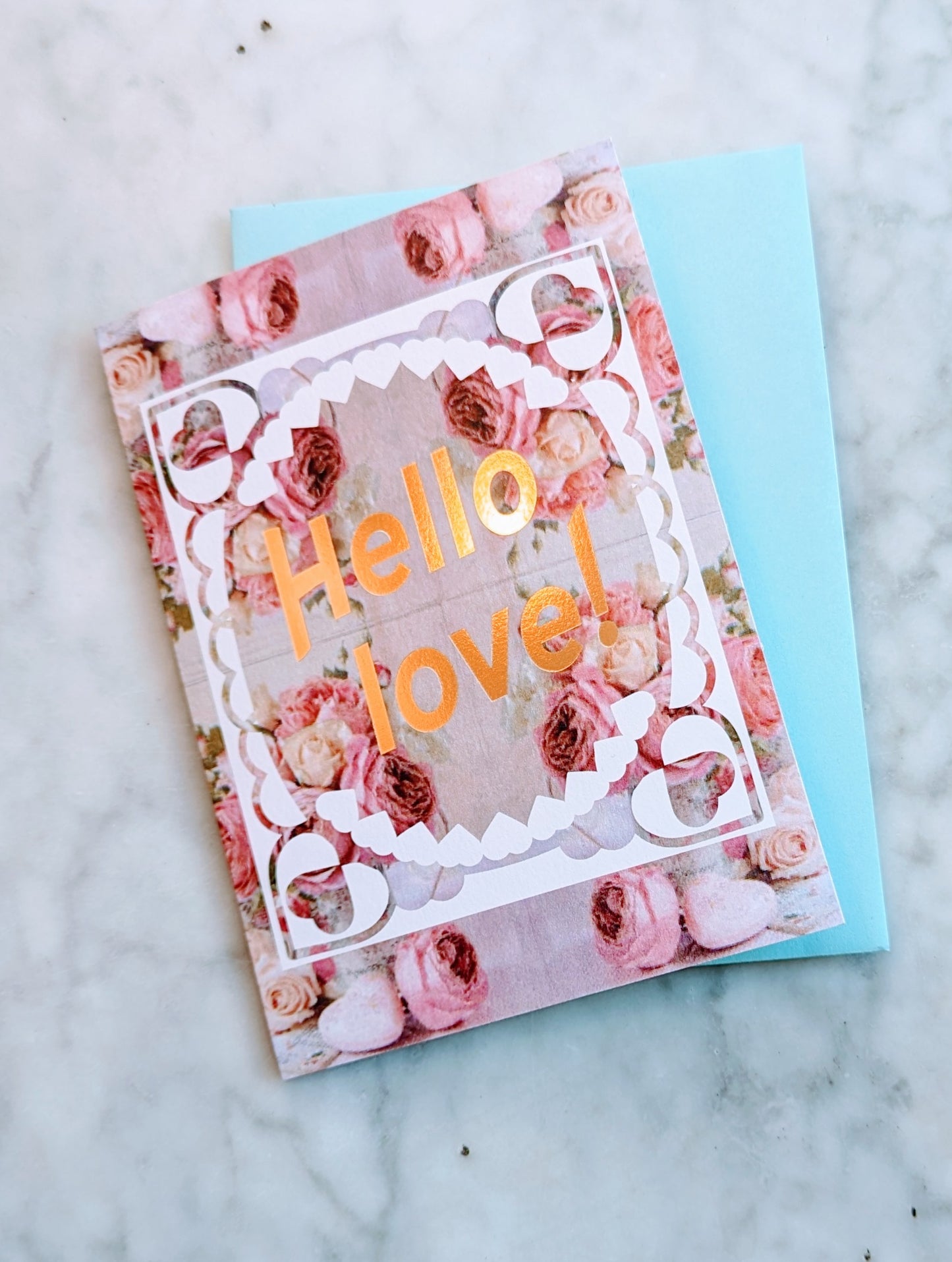 A greeting card with a floral pattern and the text 'Hello love' on it, accompanied by a sky blue envelope.