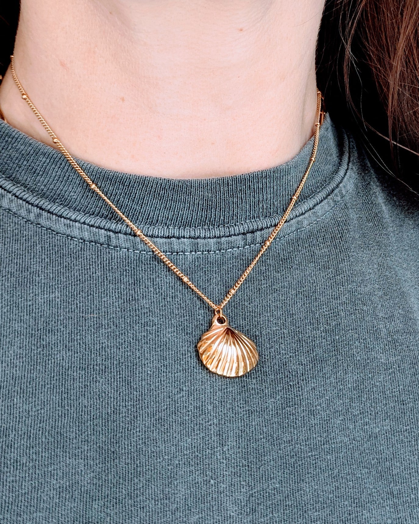 Gold necklace with a shell pendant worn by a person on a dark shirt.