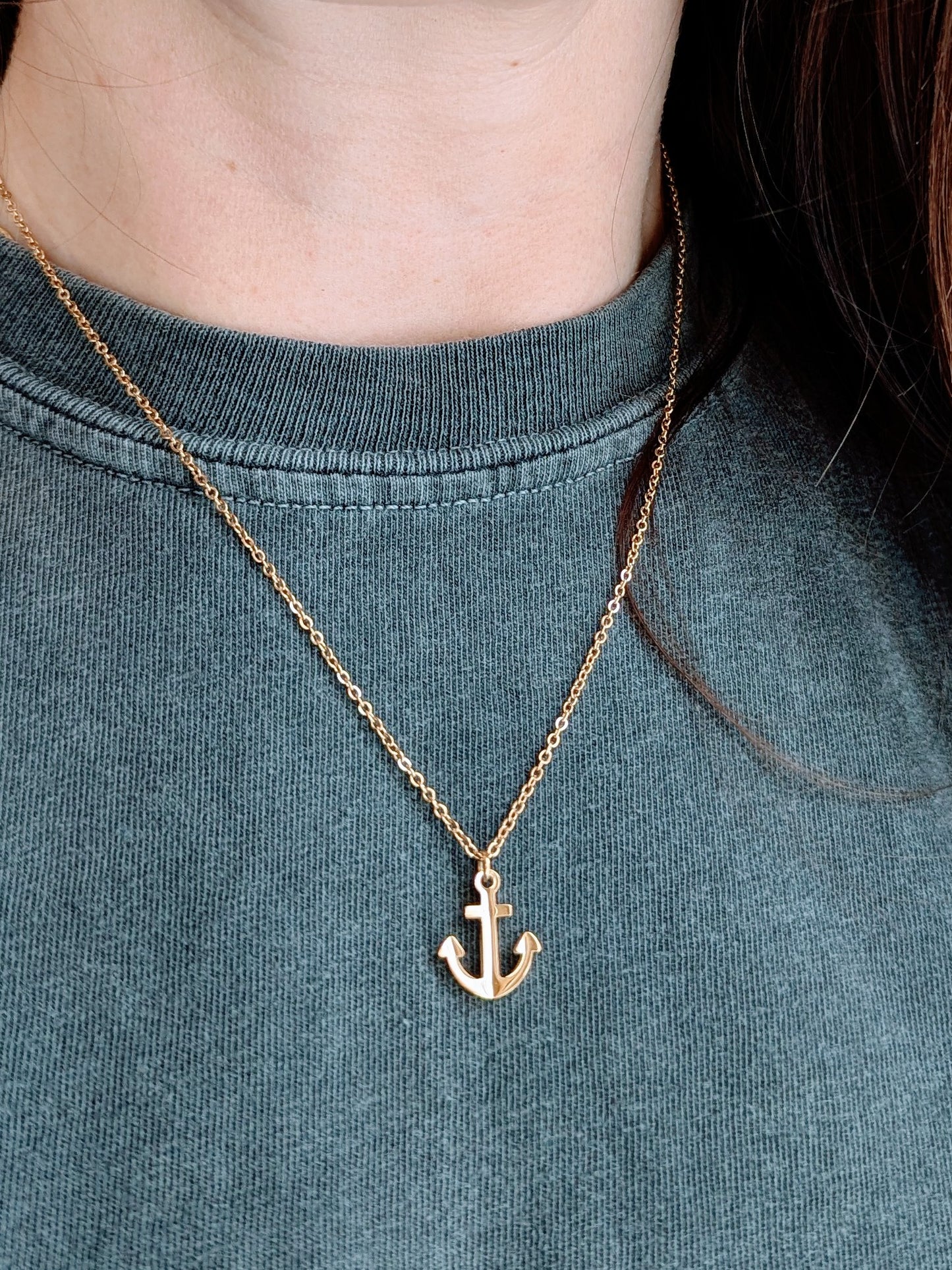 Gold anchor necklace on a person wearing a grey shirt