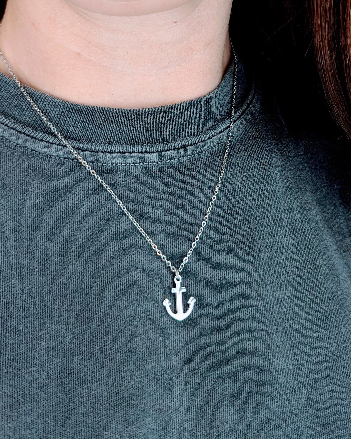 Person wearing a silver anchor necklace on a dark shirt