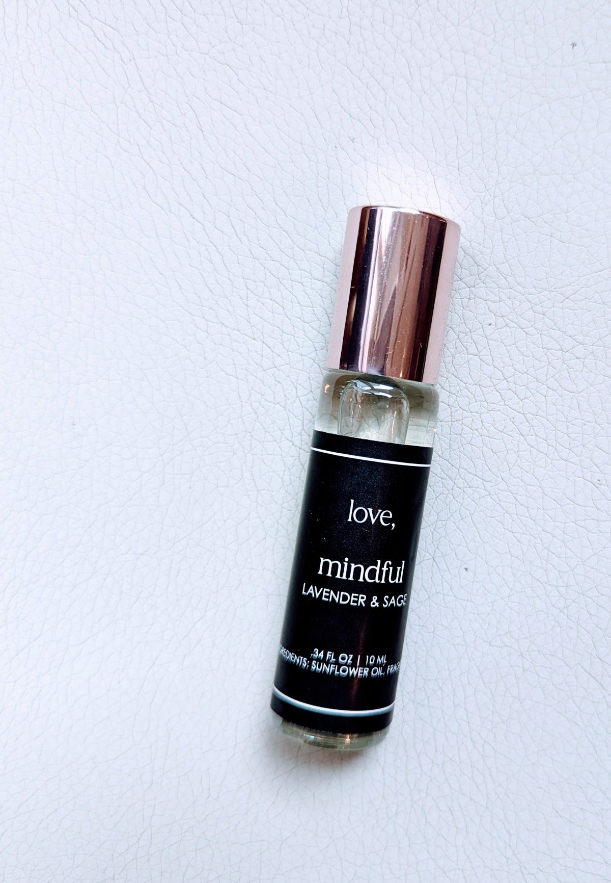 A roll-on perfume bottle with a black label that has the word 'love' written on it, along with the words 'mindful' and other text. The bottle is clear, revealing a liquid inside, and it has a metallic cap.