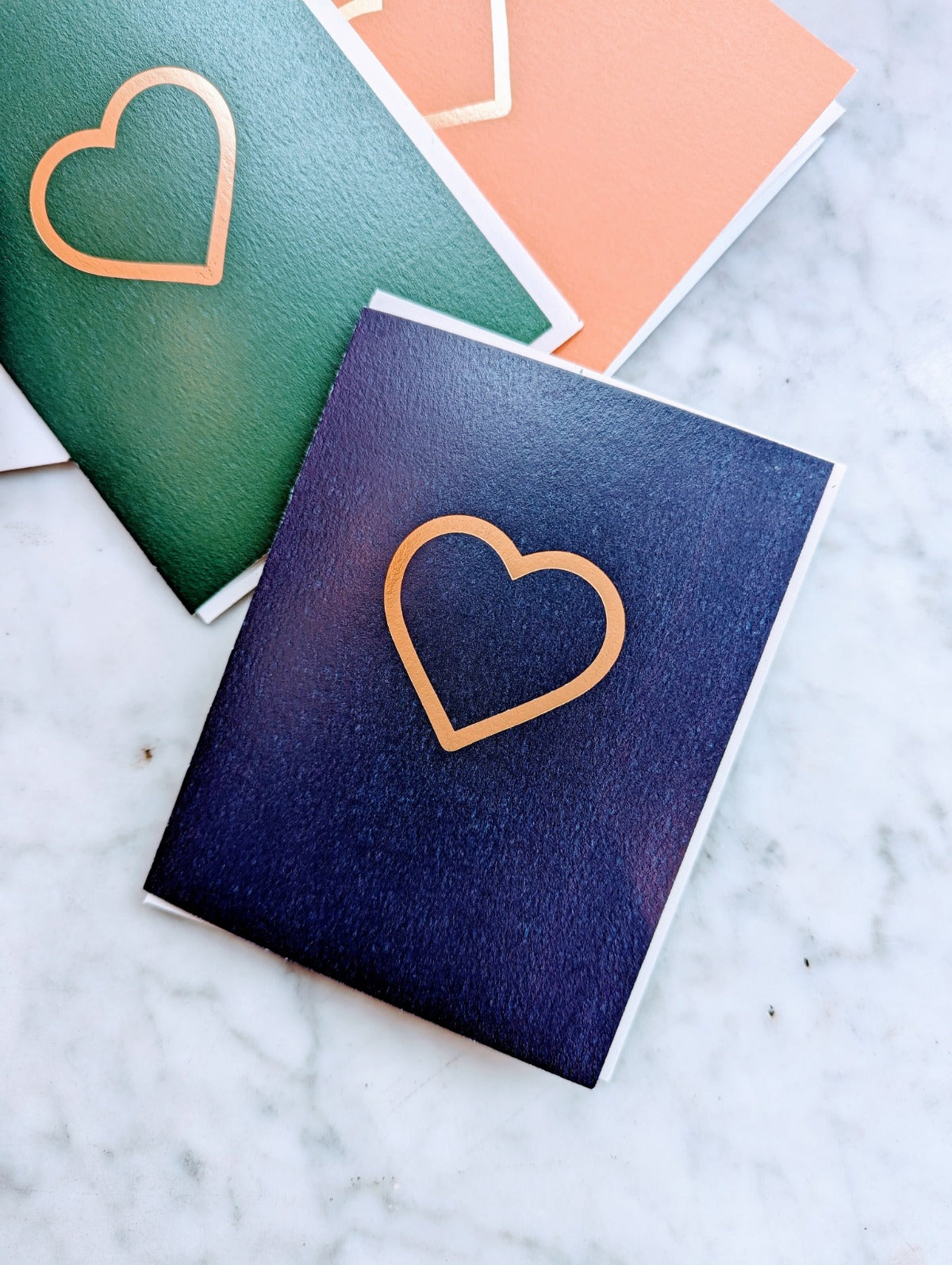 A stack of folded cards with a prominent heart shape on the front of the top card, set against a marble background.