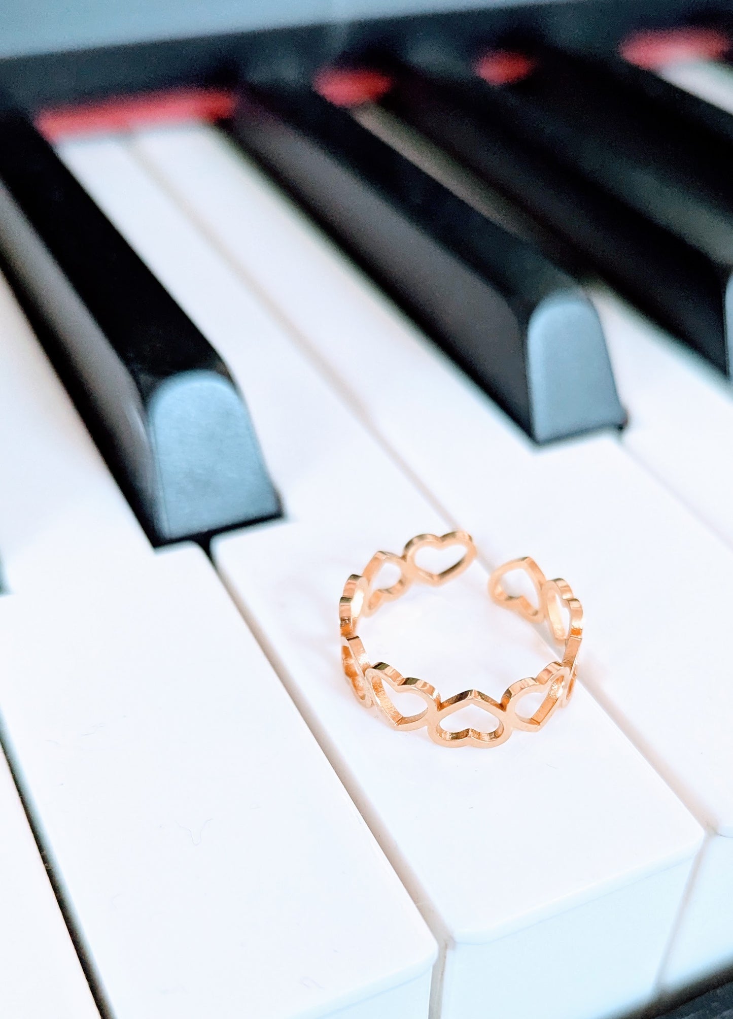 A gold-plated stainless steel ring with a design of interlinked hearts, displayed on a piano keyboard.