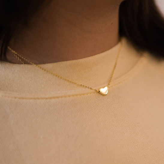 A gold-plated stainless steel floating heart necklace on a chain around a person's neck, positioned against a light-colored top.
