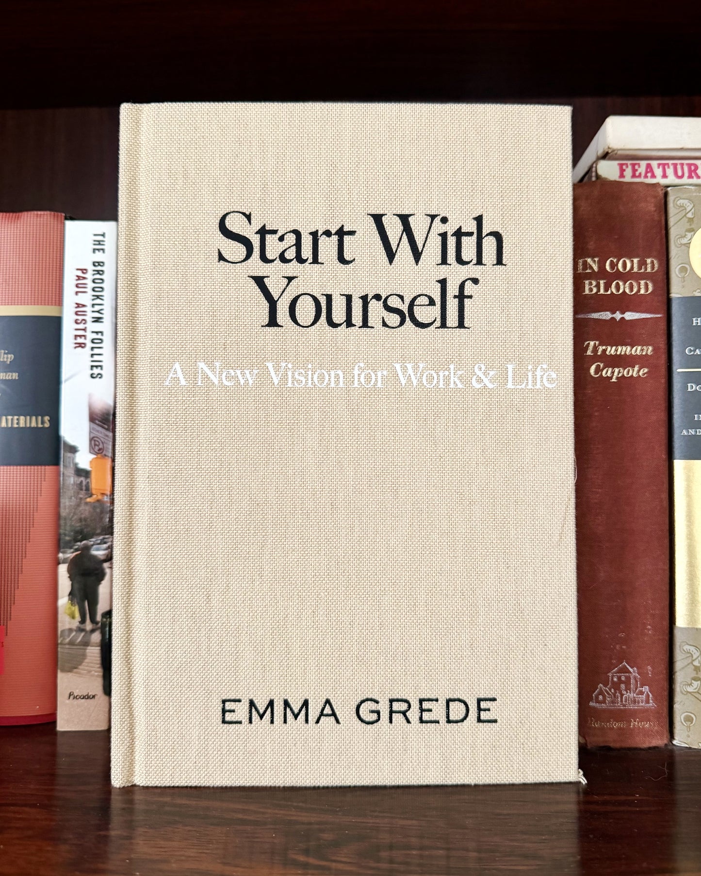 Book titled 'Start With Yourself' by Emma Grede among other books on a wooden surface.
