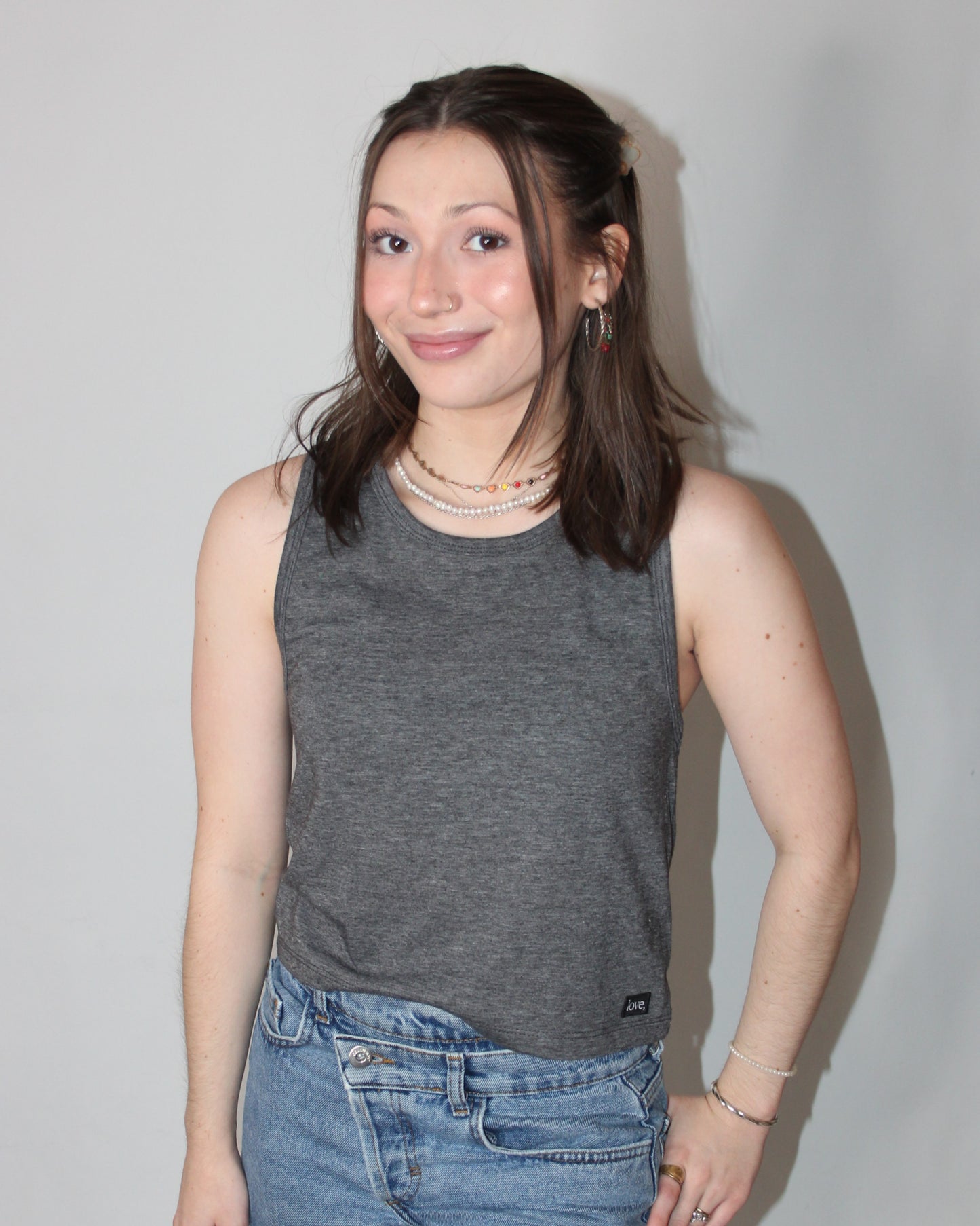 A woman wearing a gray crop tank top with a relaxed fit and sleeveless design, paired with blue denim shorts.