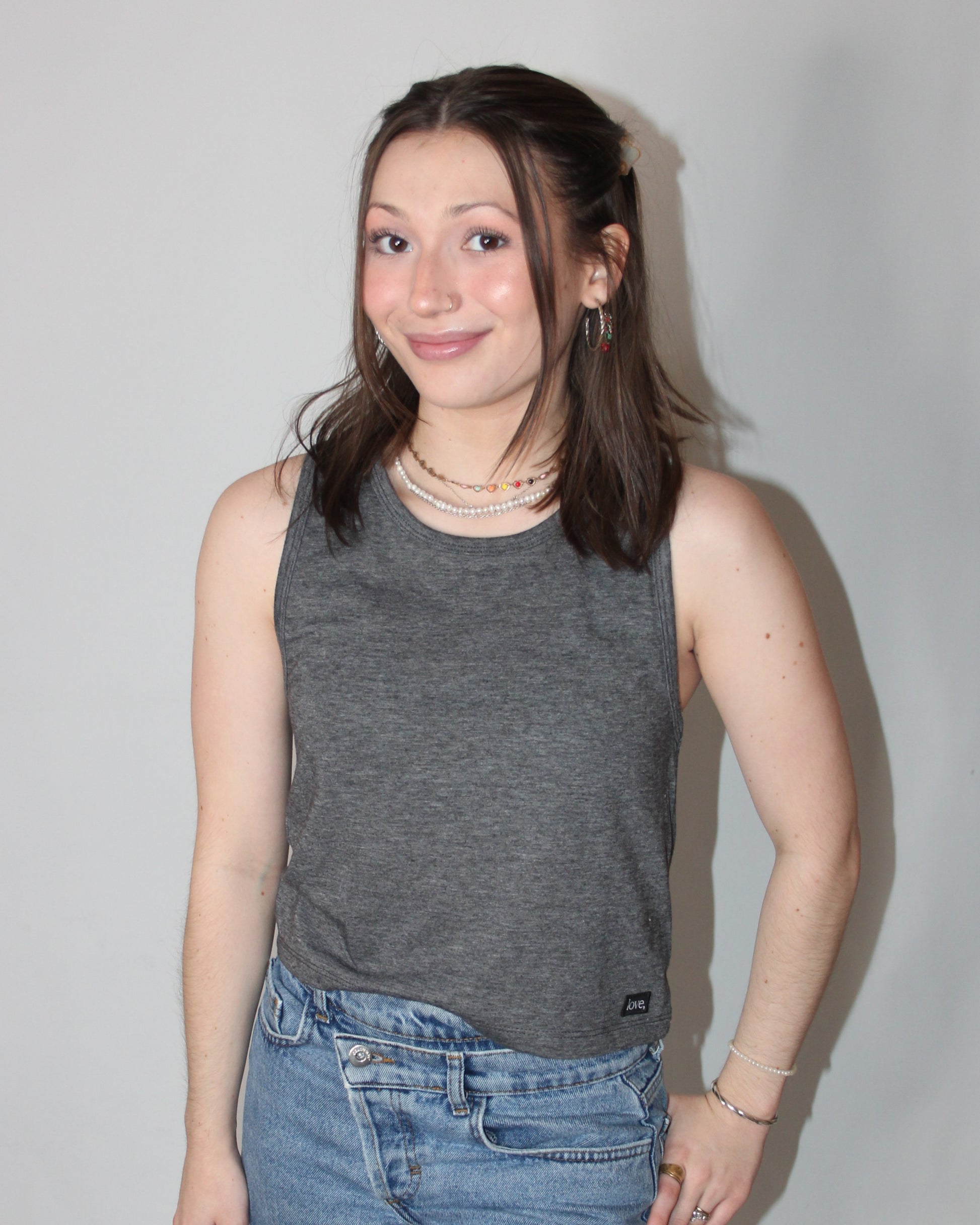 A woman wearing a gray crop tank top with a relaxed fit and sleeveless design, paired with blue denim shorts.