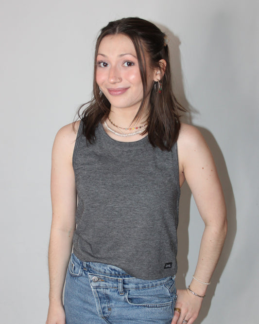 A woman wearing a gray crop tank top with a relaxed fit and sleeveless design, paired with blue denim shorts.