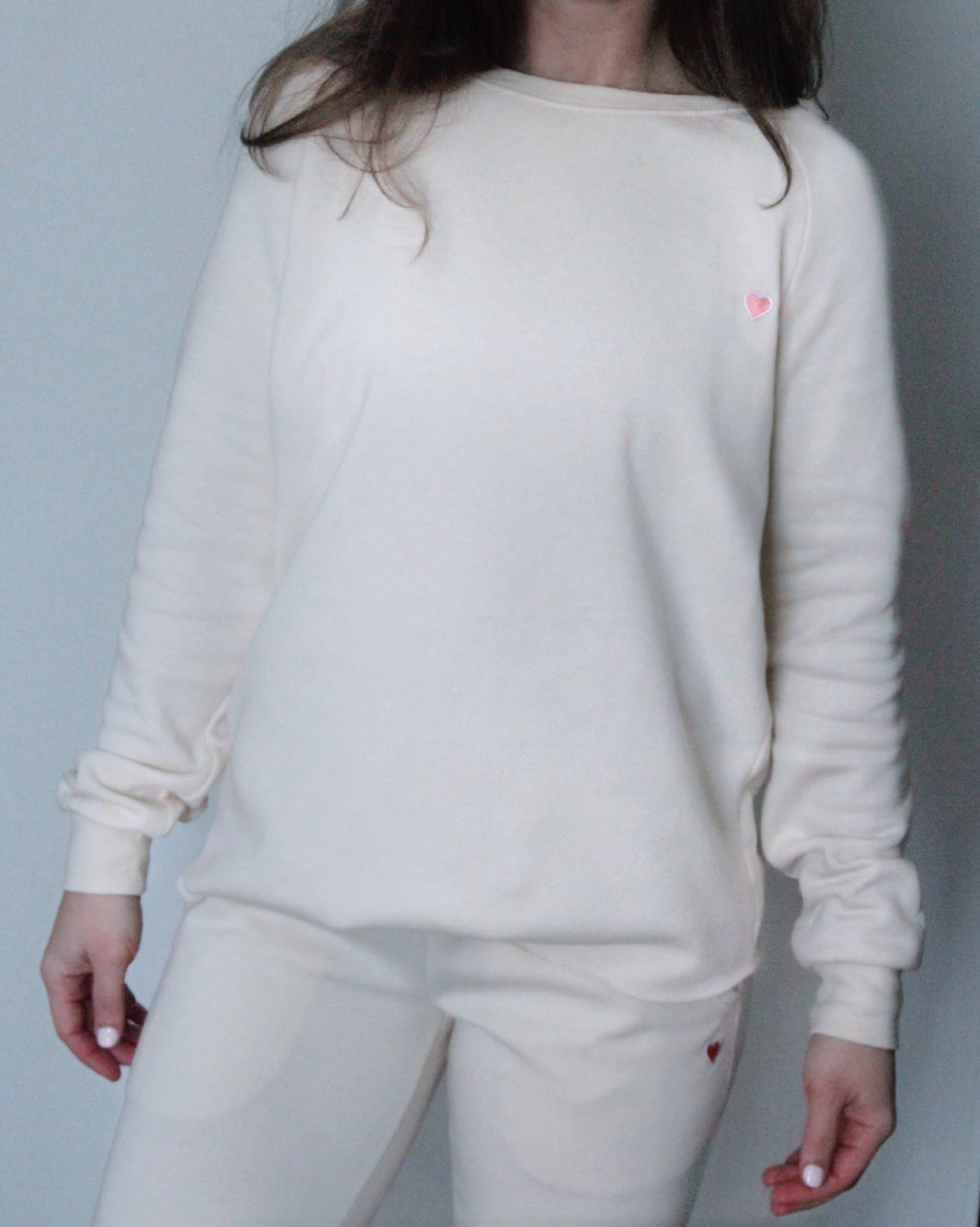 A person wearing a beige long-sleeved t-shirt with a pink patch on the left chest area.
