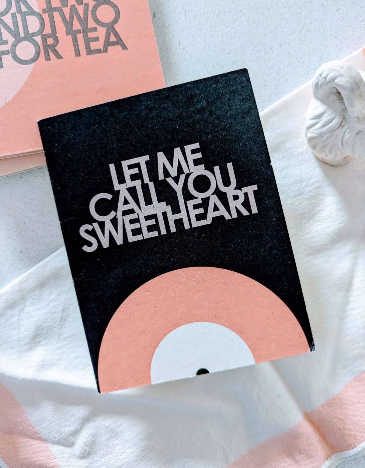 A greeting card with the text 'LET ME CALL YOU SWEETHEART' printed on it, featuring a black background with a gradient of colors leading to white at the bottom.