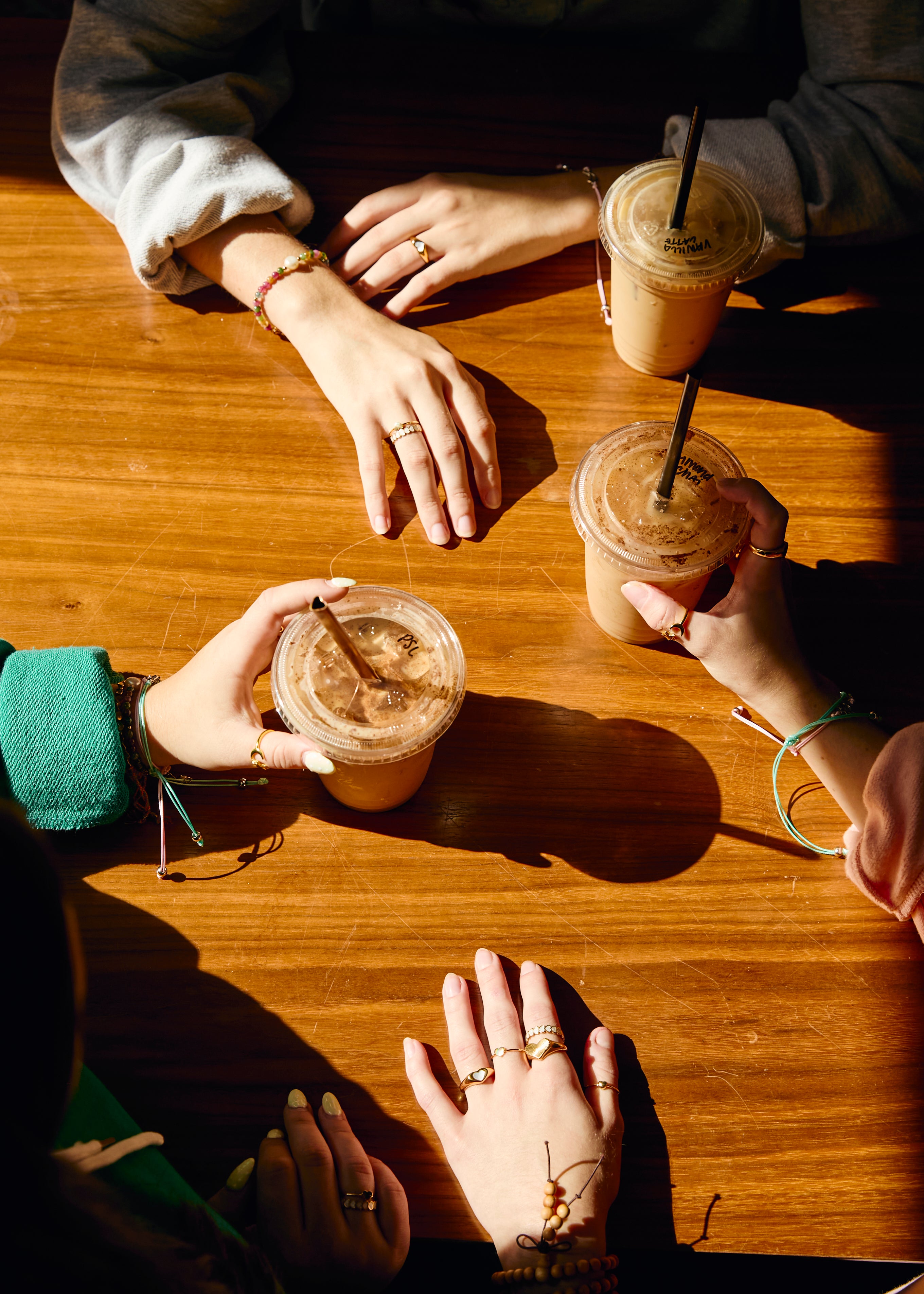 Four people holding iced drinks with straws on a wooden table