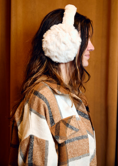 Person wearing white fluffy earmuffs with a brown and beige patterned coat against a plain background