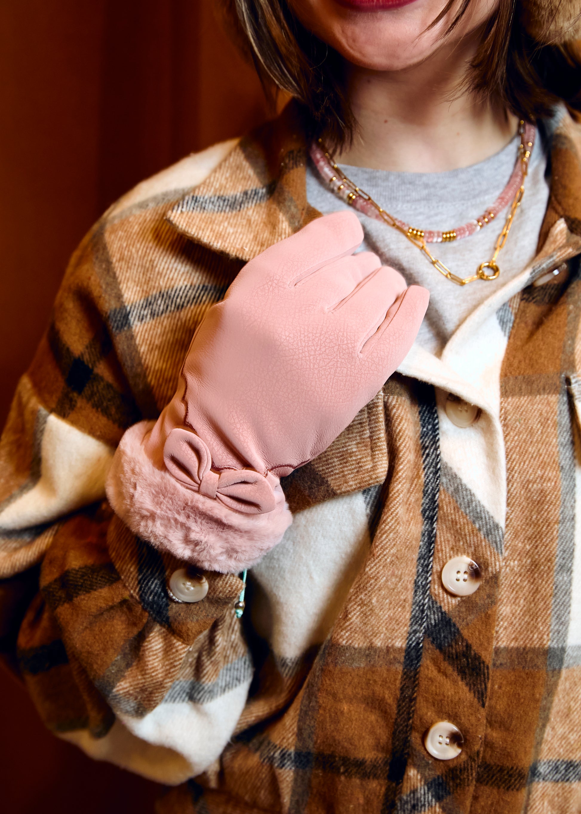 Person wearing a plaid coat with a pink glove, holding a small pink bag.