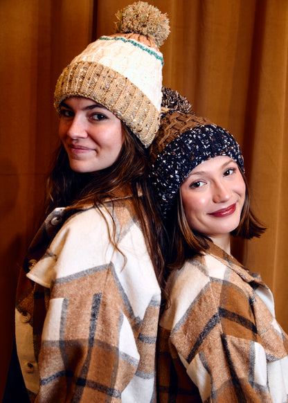 Two women wearing winter hats and plaid scarves against a brown background