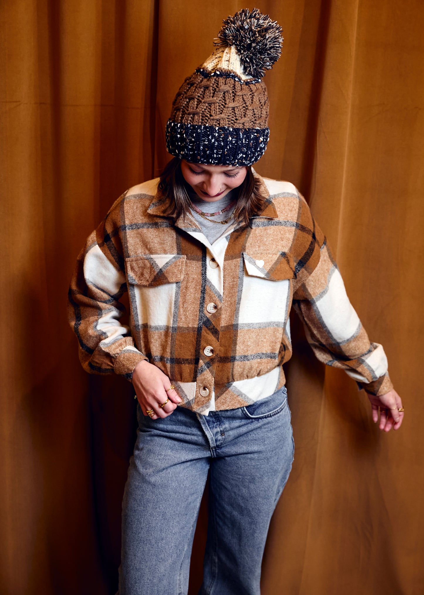 Person wearing a plaid shirt, jeans, and a patterned beanie against a wooden background