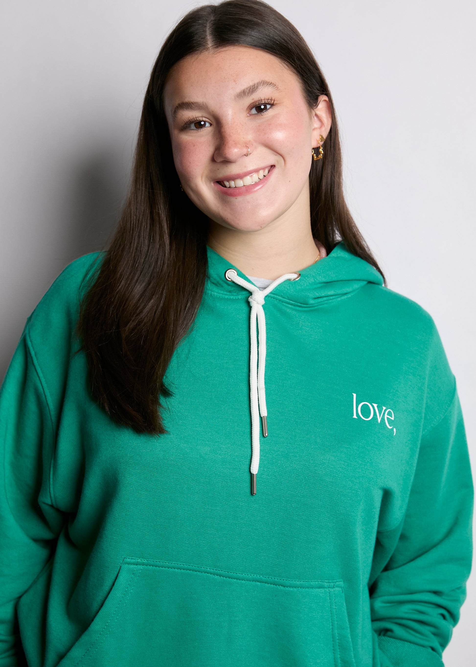 Person wearing a green hoodie with 'love,' printed on it against a plain background