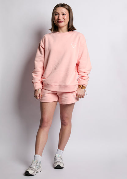 Person wearing a pink sweatshirt and shorts set on a plain background