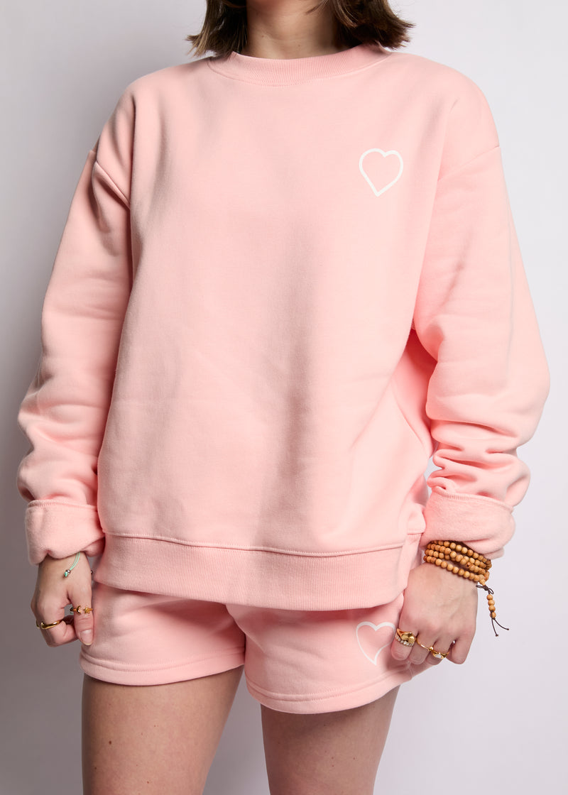 Person wearing a pink sweatshirt and shorts set with a heart logo on a plain background