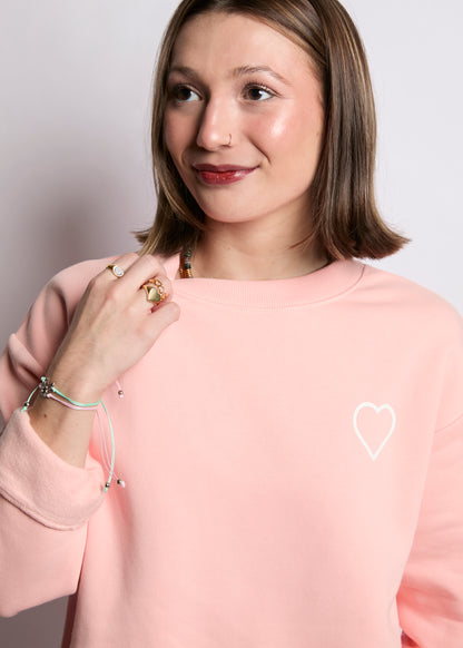 Woman wearing a pink sweatshirt with a heart design on a plain background