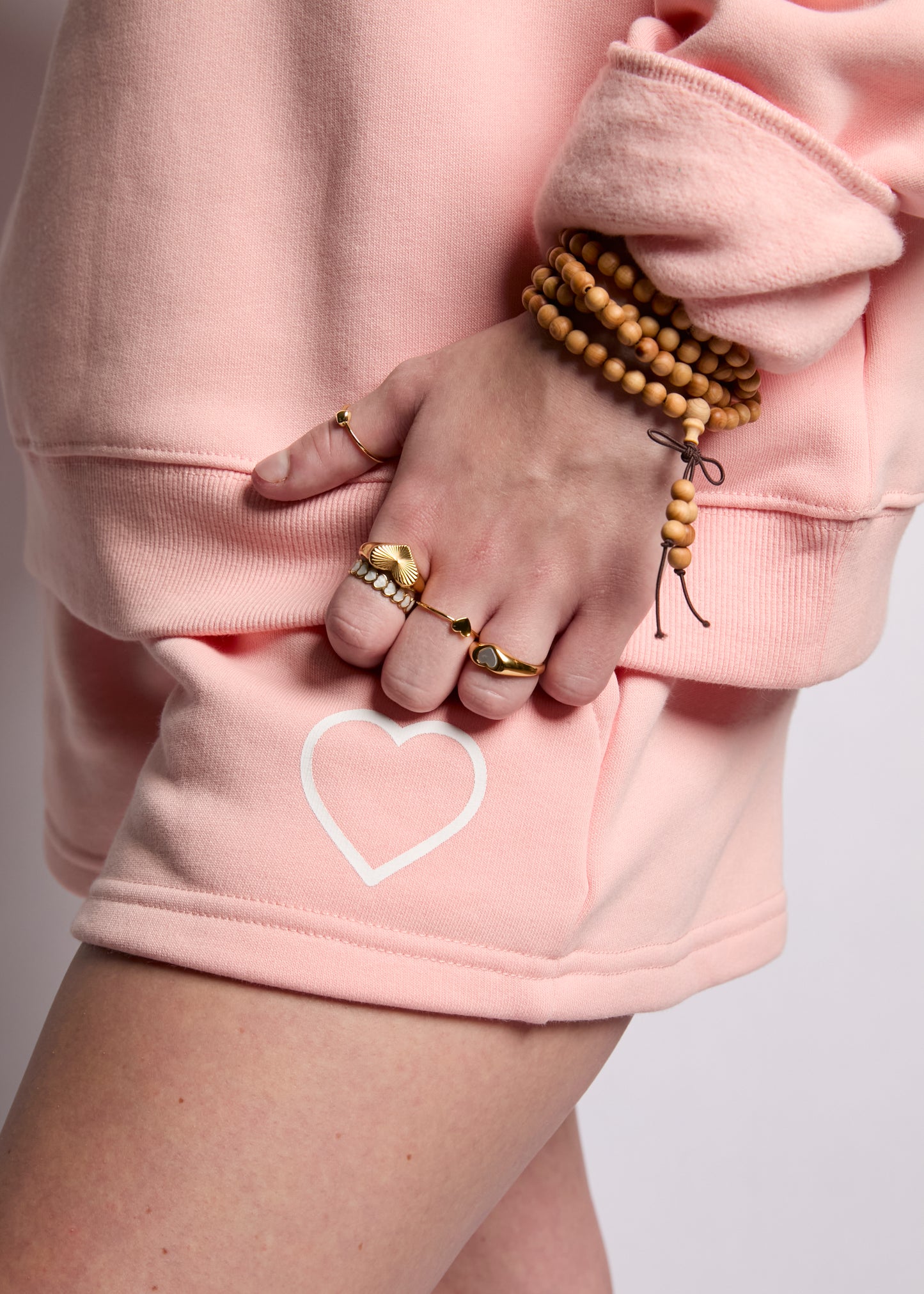 Person wearing a pink sweatshirt with a heart design, gold rings, and a wooden bracelet.
