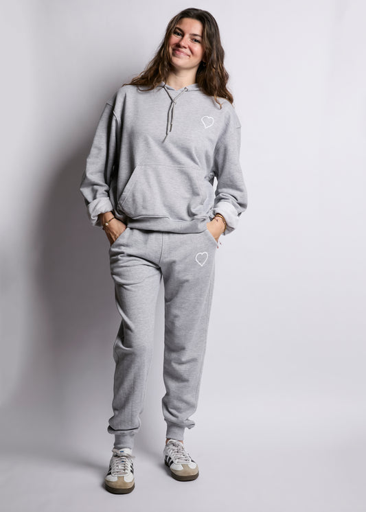 Person wearing a gray sweatshirt and pants with heart designs on a plain background