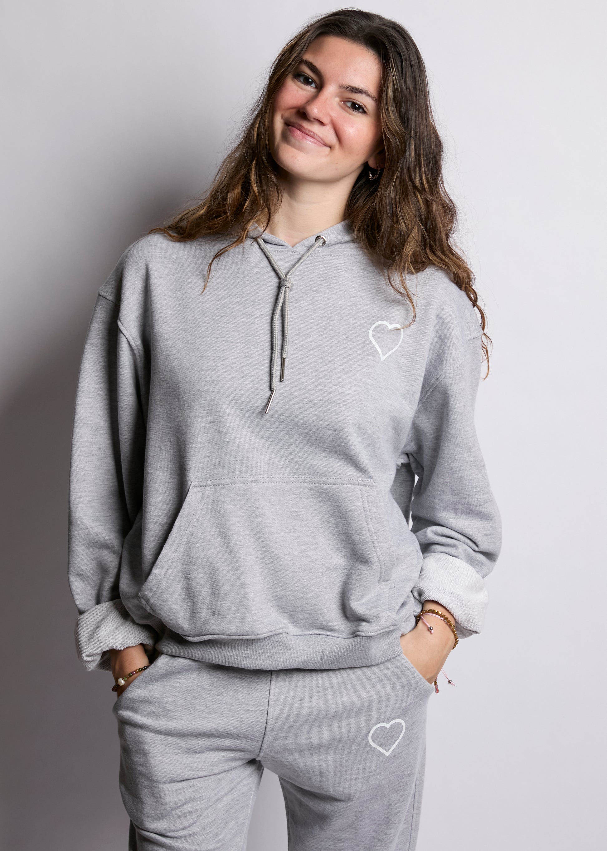 Woman wearing a gray hoodie and pants with heart designs on a plain background