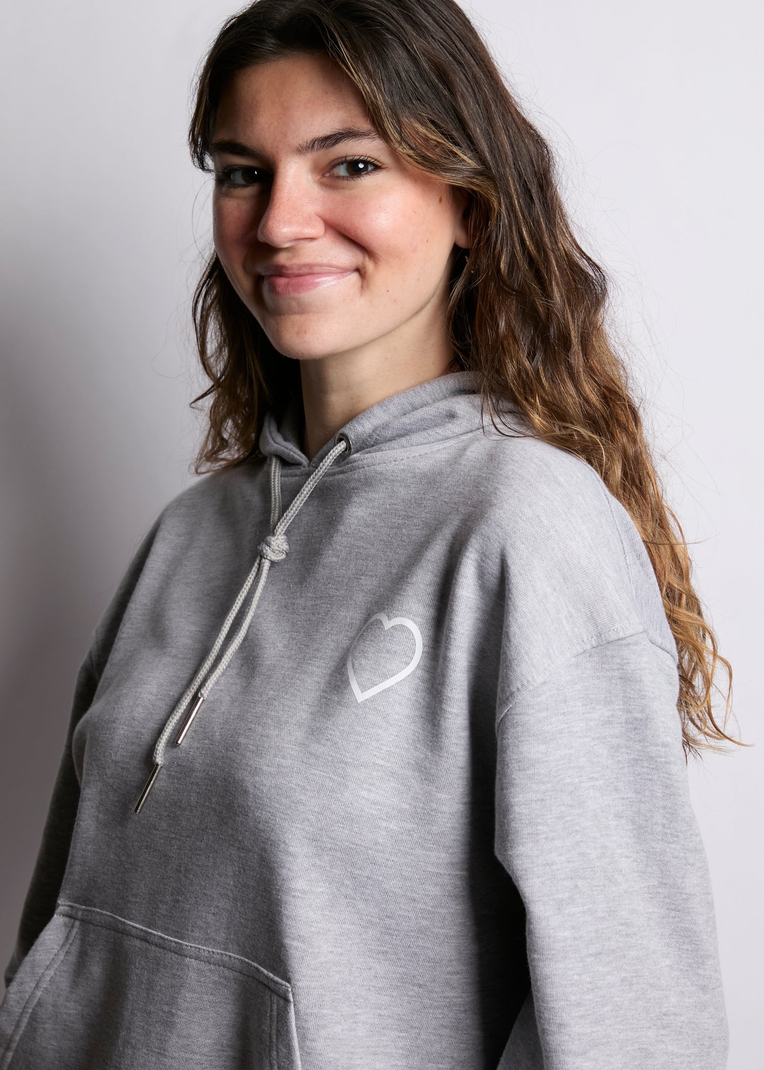 Woman wearing a gray hoodie with a heart design on a plain background