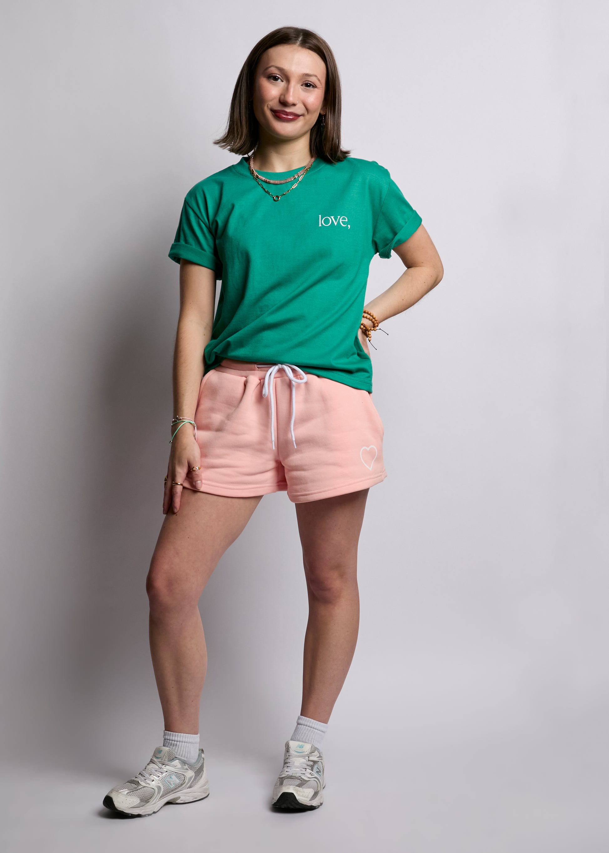 Person wearing a green t-shirt with 'LOVE' and pink shorts on a plain background