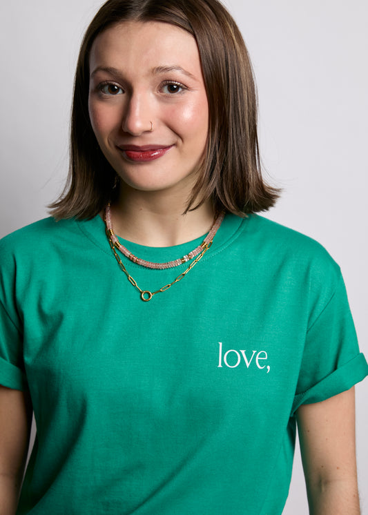 Person wearing a green t-shirt with 'love,' printed on it against a plain background