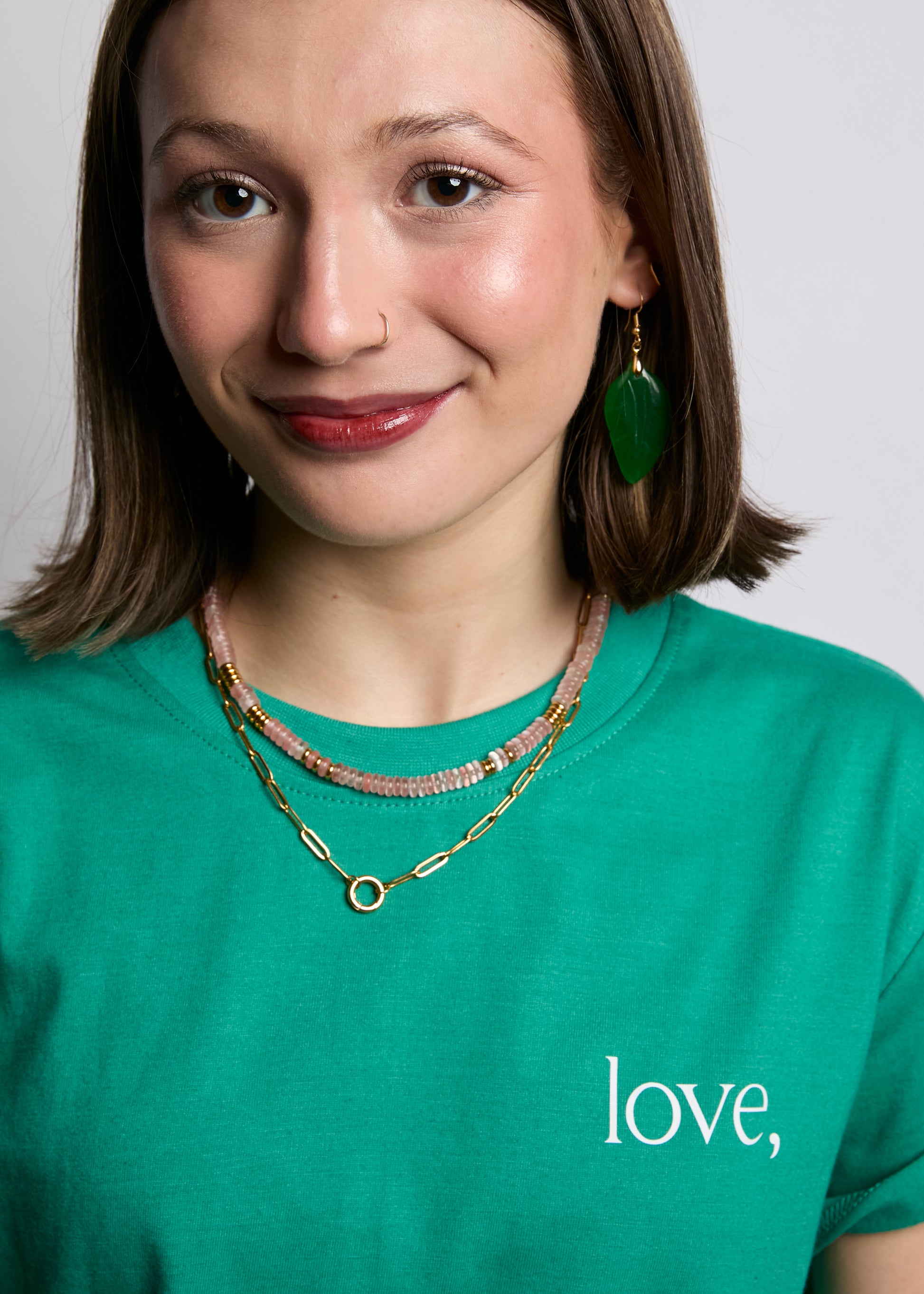 Woman wearing a green shirt with 'love,' text and gold jewelry against a plain background