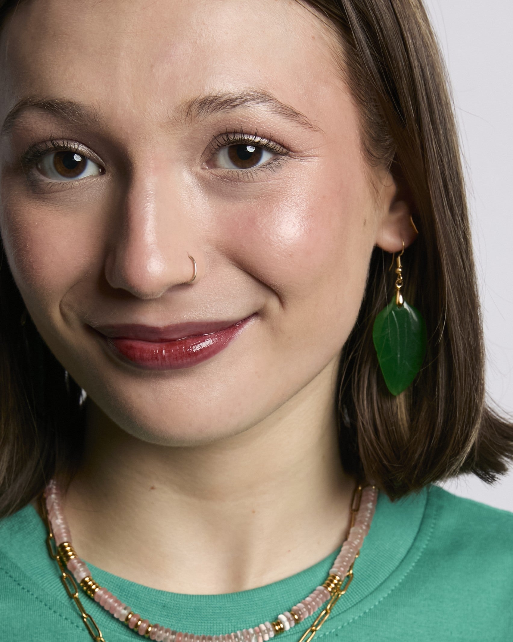 Close-up of a woman wearing green earrings and a necklace with a white background