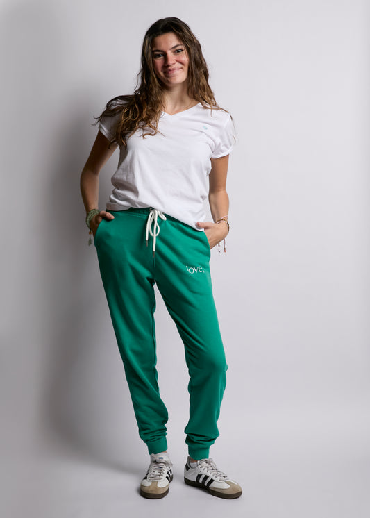 Woman wearing a white t-shirt and green sweatpants against a plain background