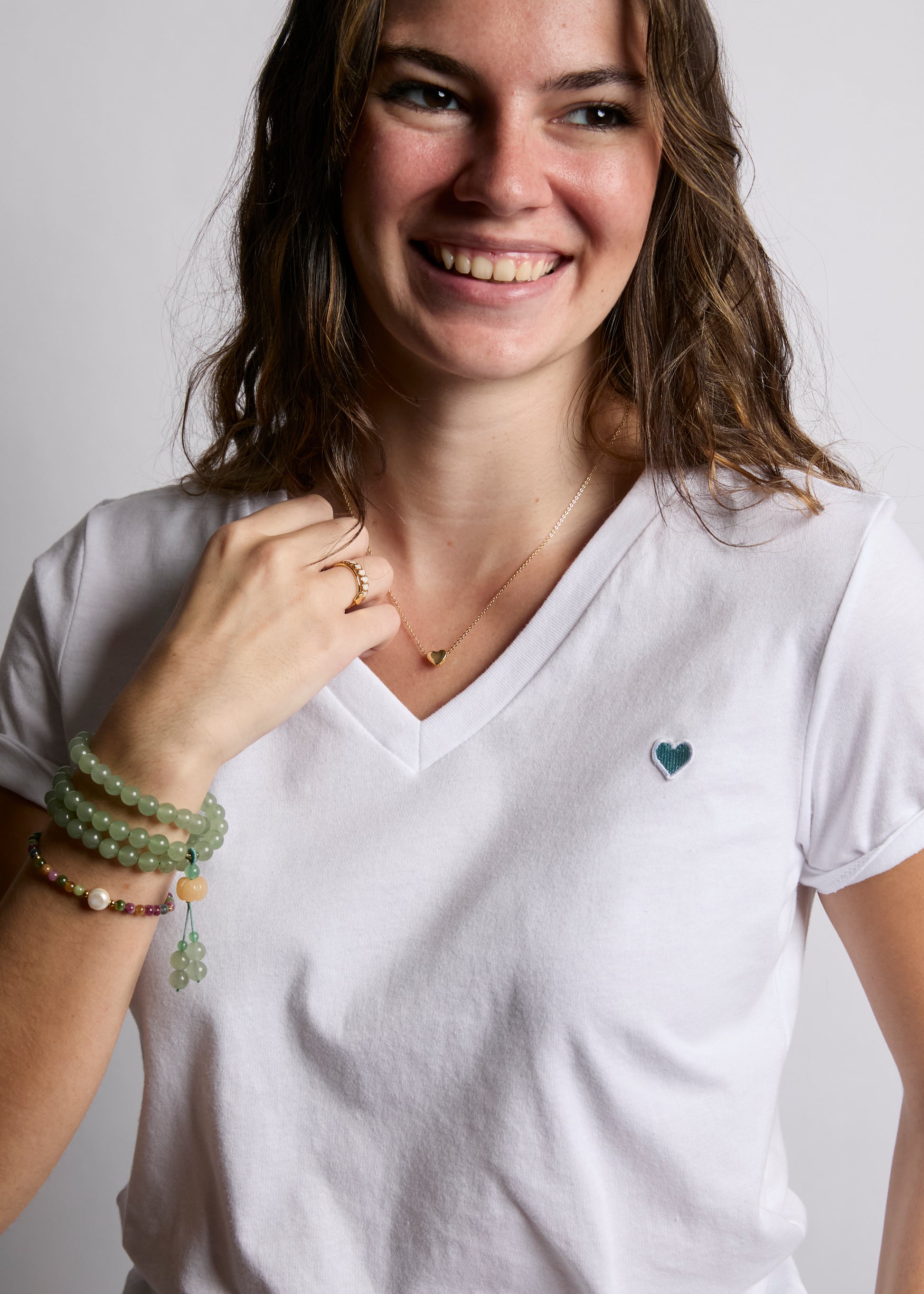Woman wearing a white t-shirt with a small heart design, smiling against a plain background.