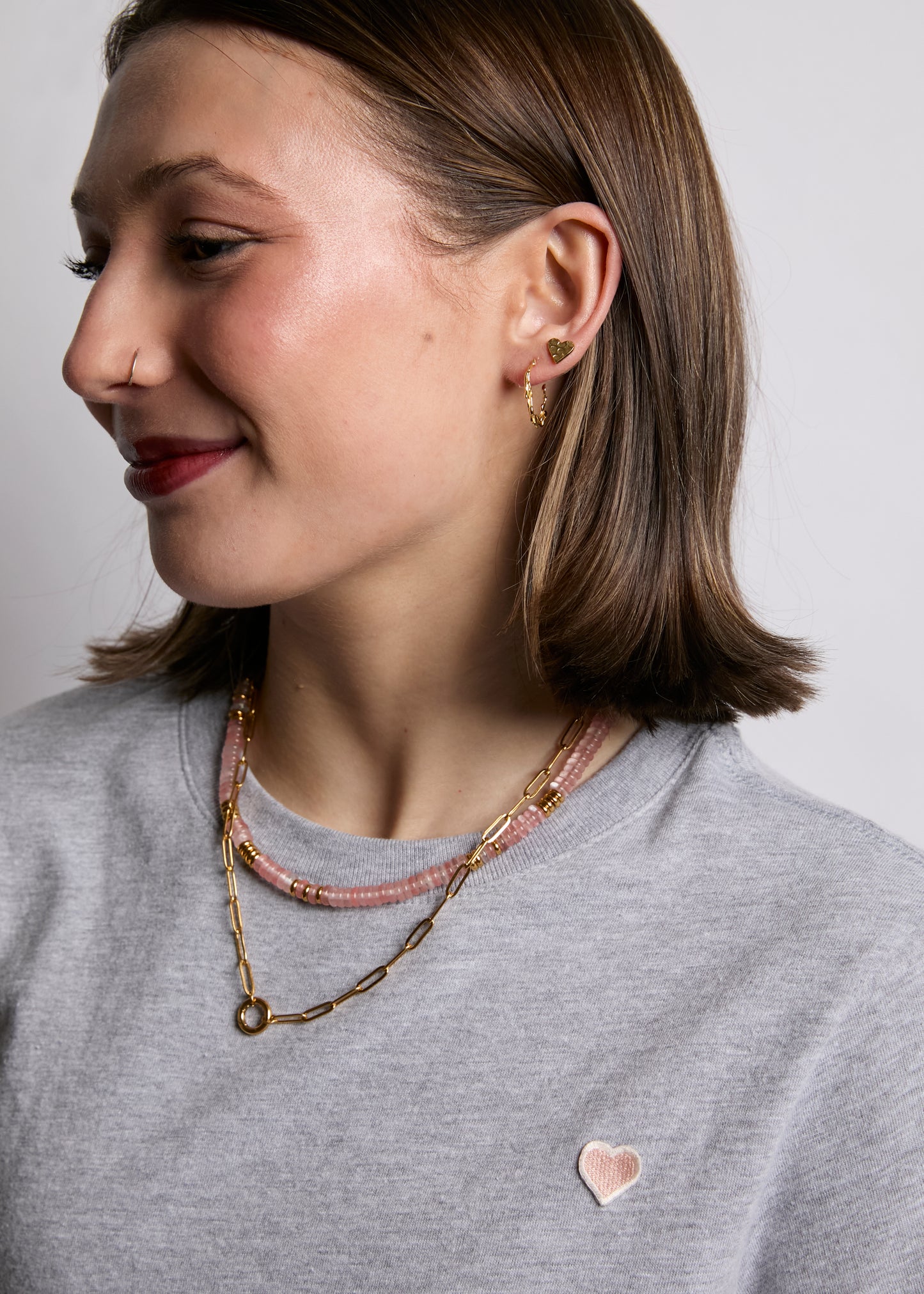 Woman wearing layered necklaces and earrings against a neutral background