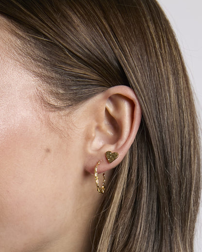 Close-up of an ear wearing gold hoop earrings with a heart charm.