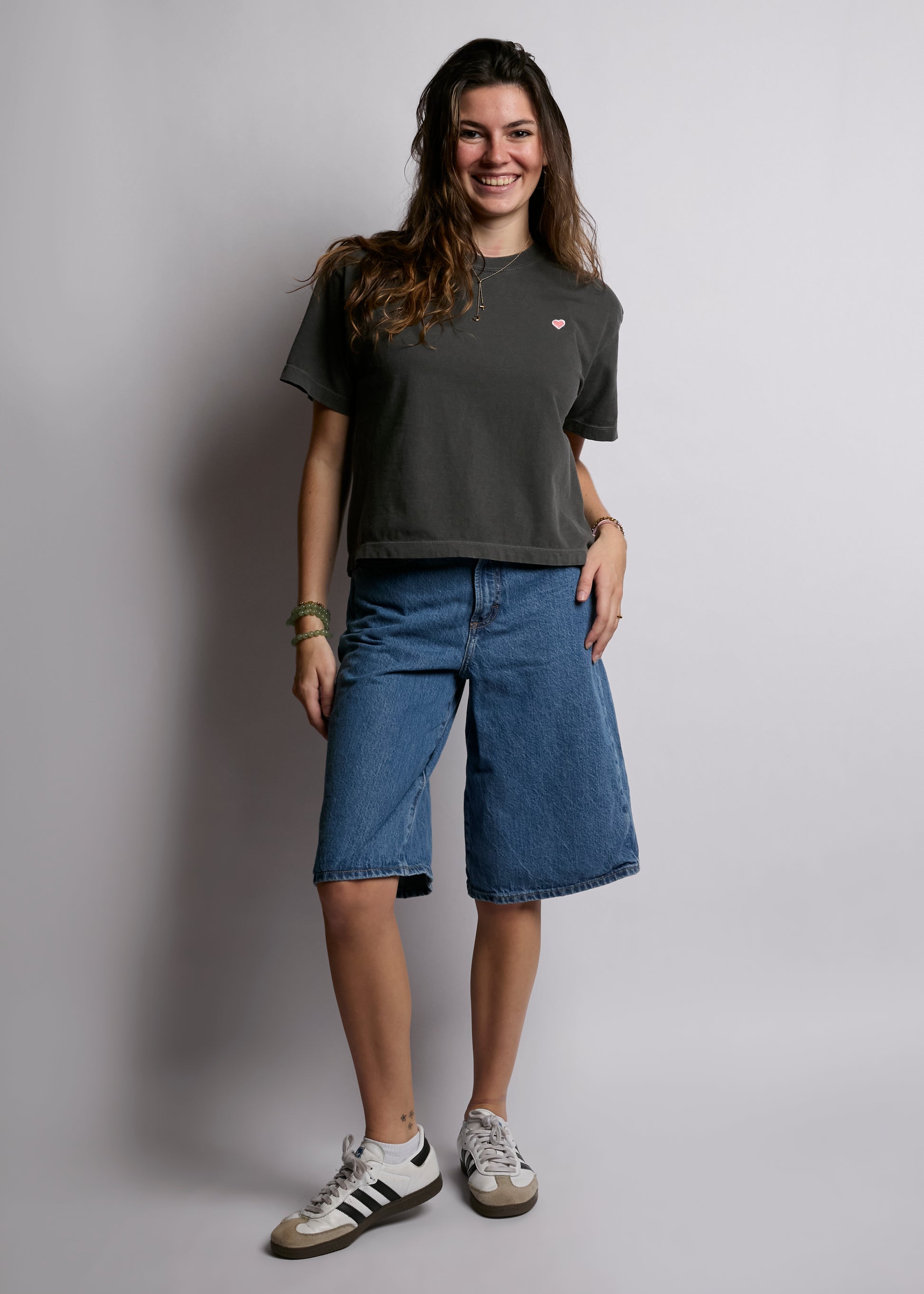 Woman wearing a dark gray t-shirt and blue denim shorts against a plain background