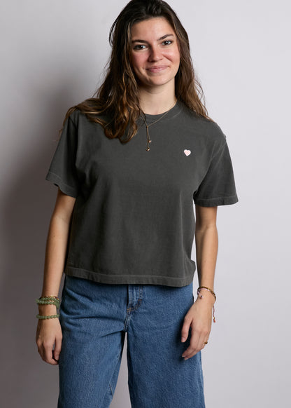 Person wearing a dark gray t-shirt with a small pink heart design on a plain background