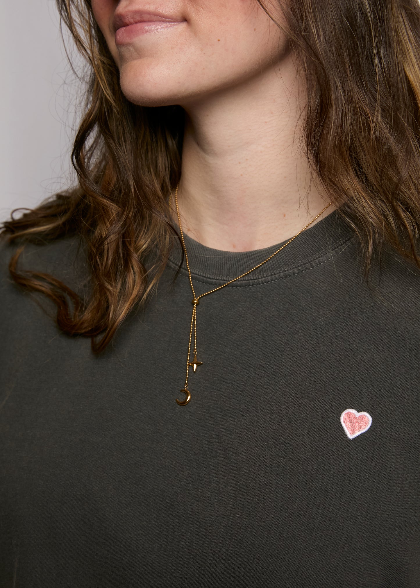 Woman wearing a gold necklace with a heart pendant on a dark shirt.