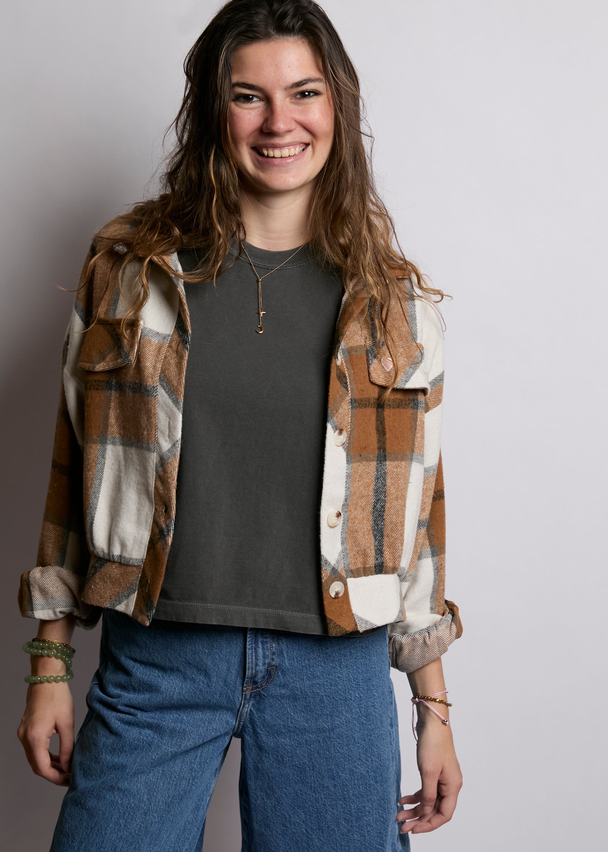 Person wearing a plaid shirt over a dark top with blue jeans on a plain background