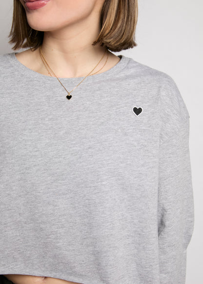 Person wearing a gray sweatshirt with a heart design on a plain background