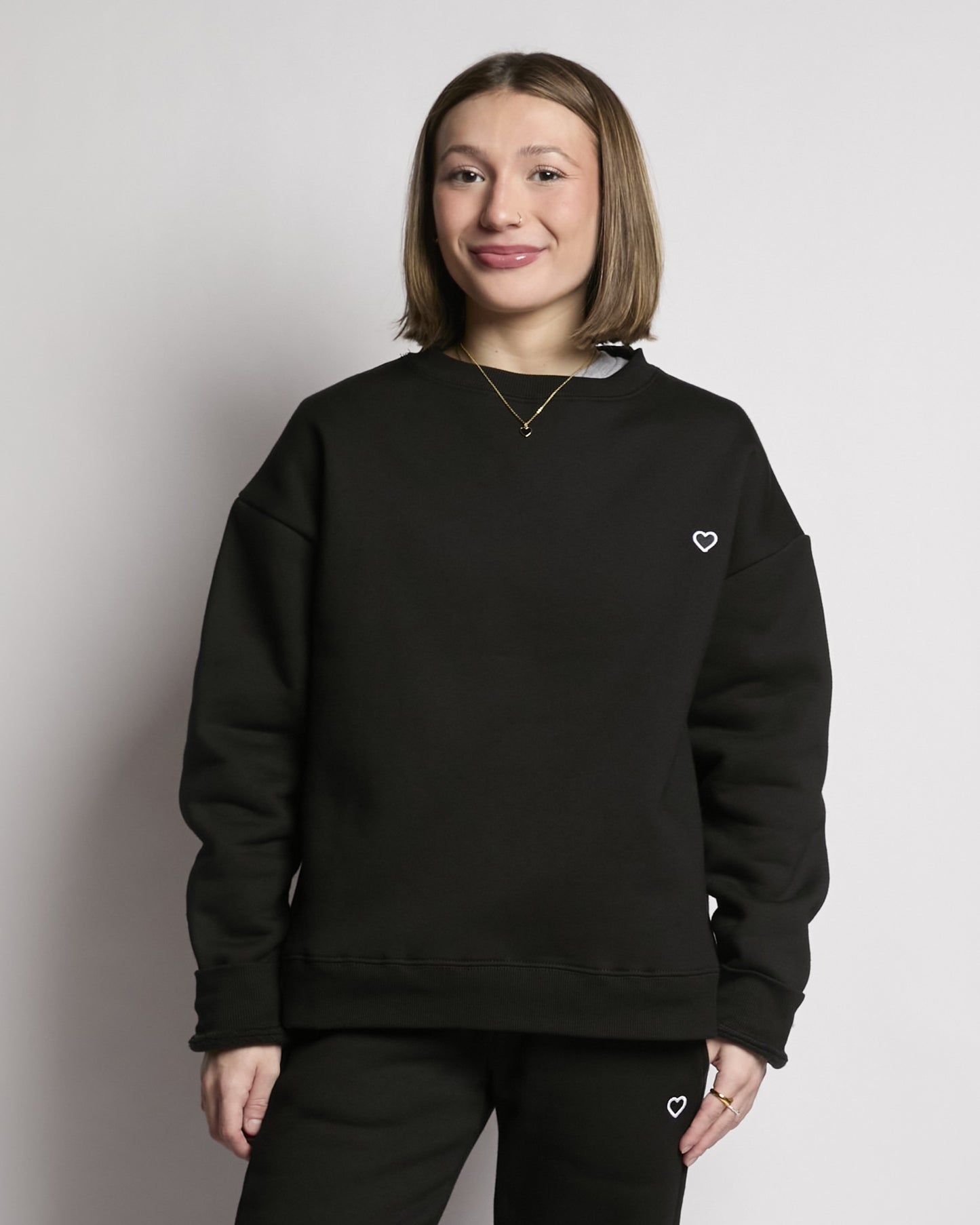 Person wearing a black sweatshirt with a heart logo on a plain background