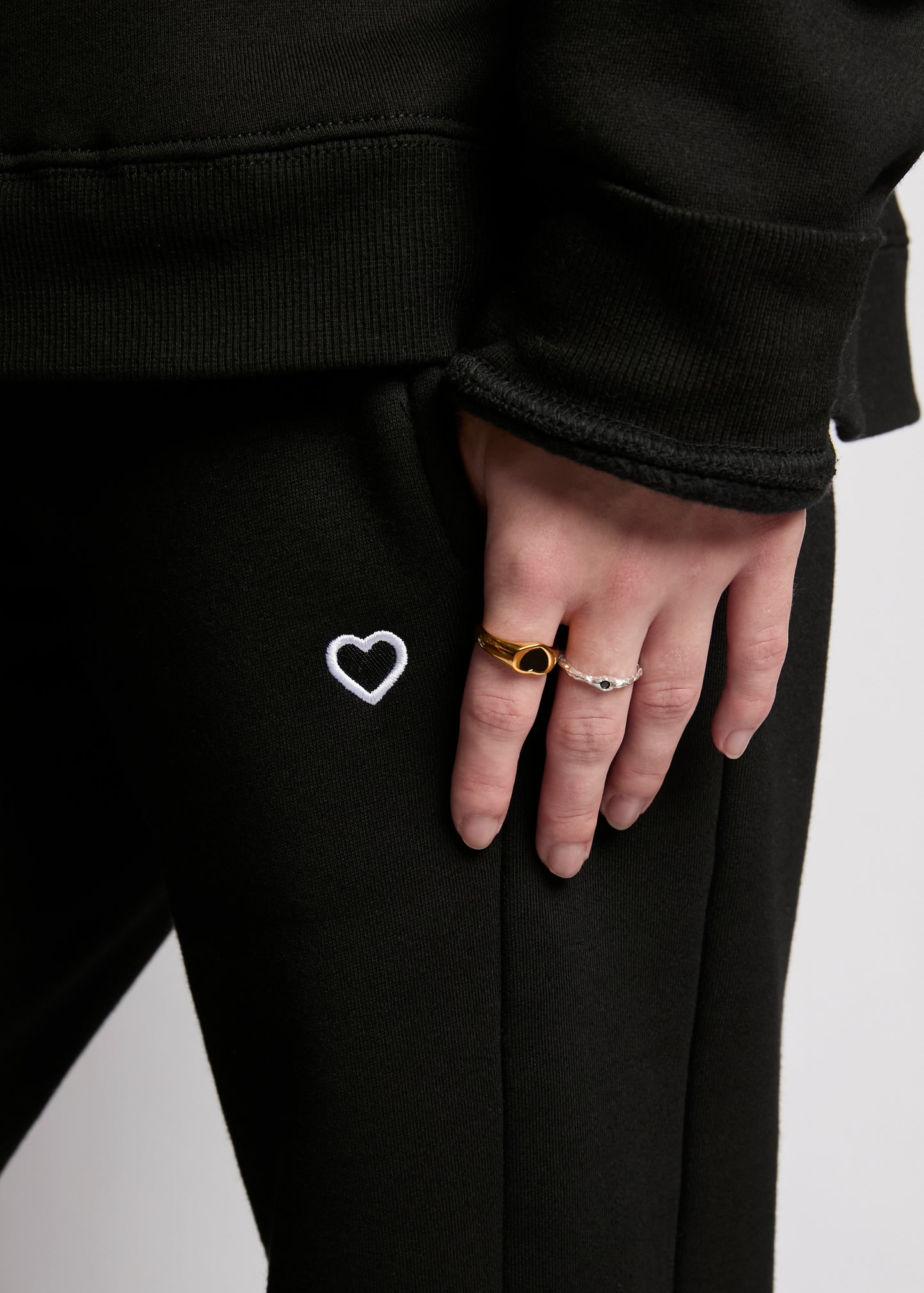 Person wearing black pants with a heart design, holding hands with another person on a light gray background.