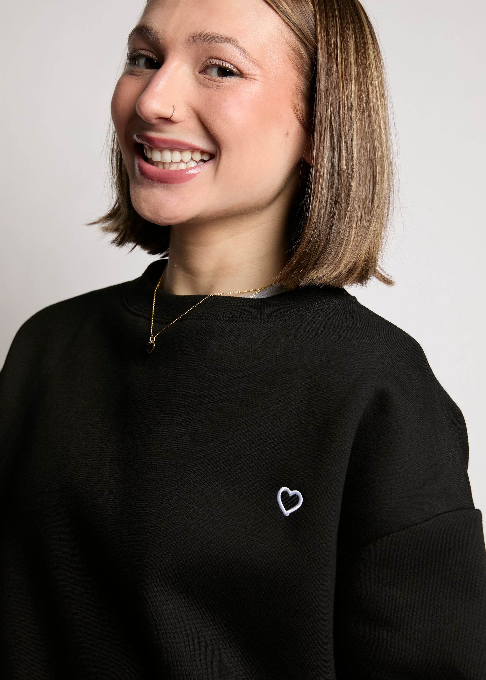 Person wearing a black sweatshirt with a heart design on a plain background