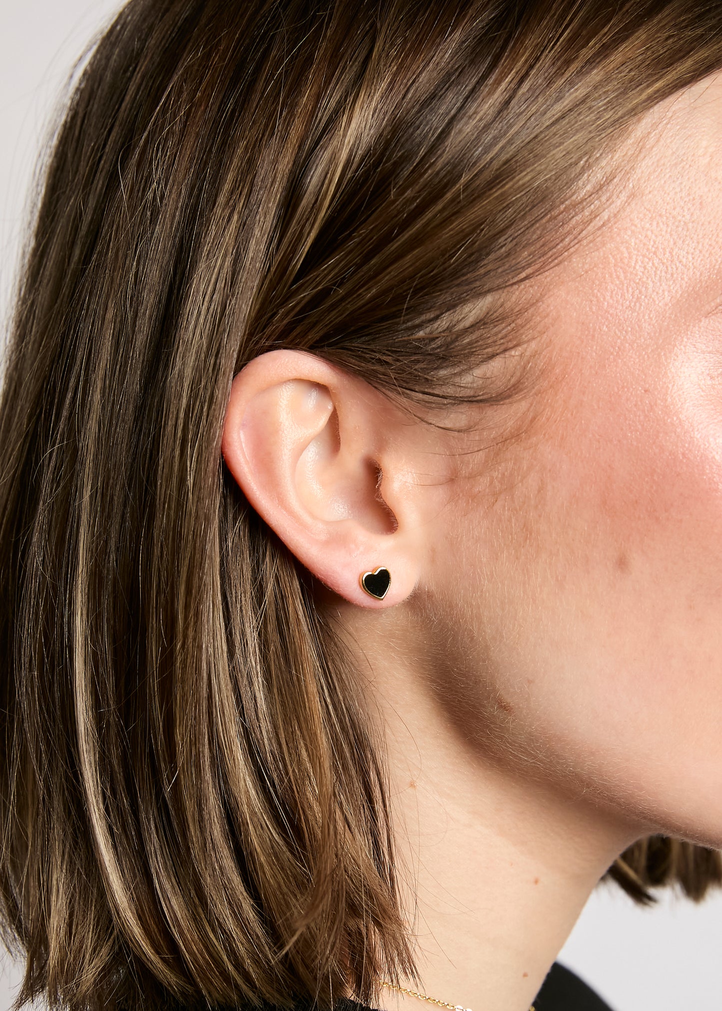 Close-up of an ear with a black stud earring on a neutral background