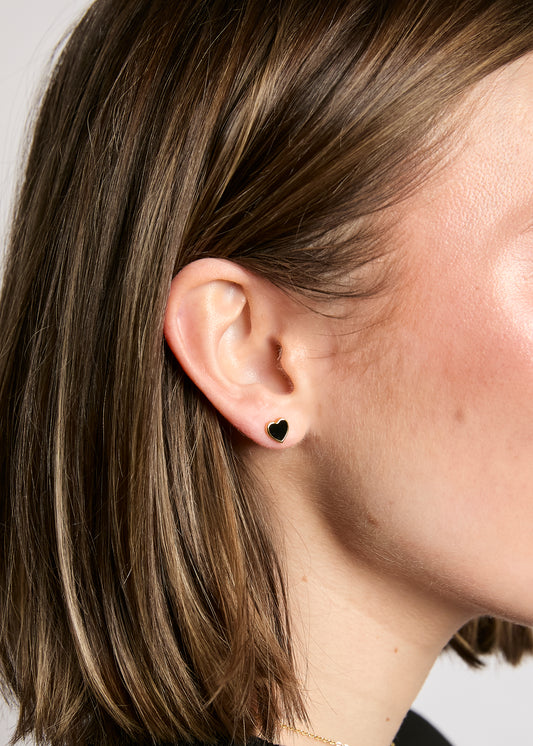 Close-up of an ear with a black stud earring on a neutral background