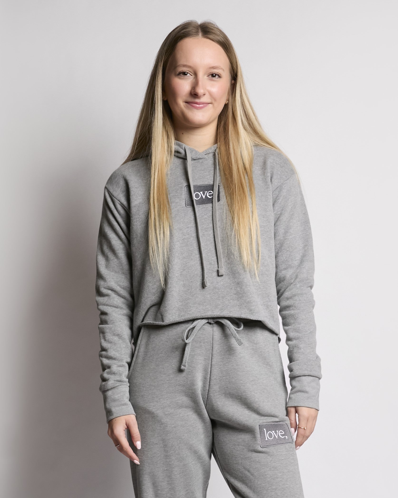 Person wearing a gray hoodie and pants with 'love' branding on a plain background